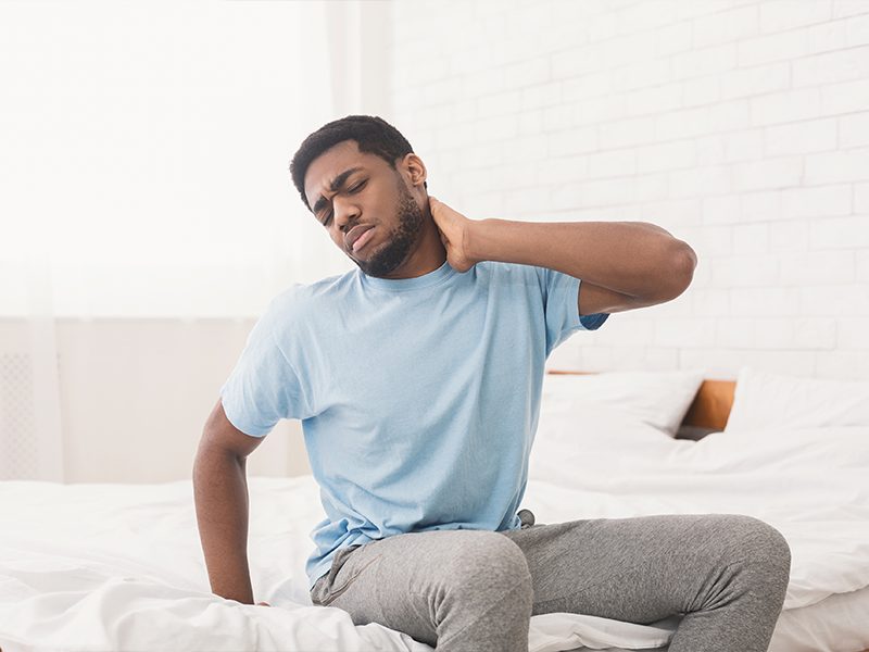 man sitting on bed holding neck in pain