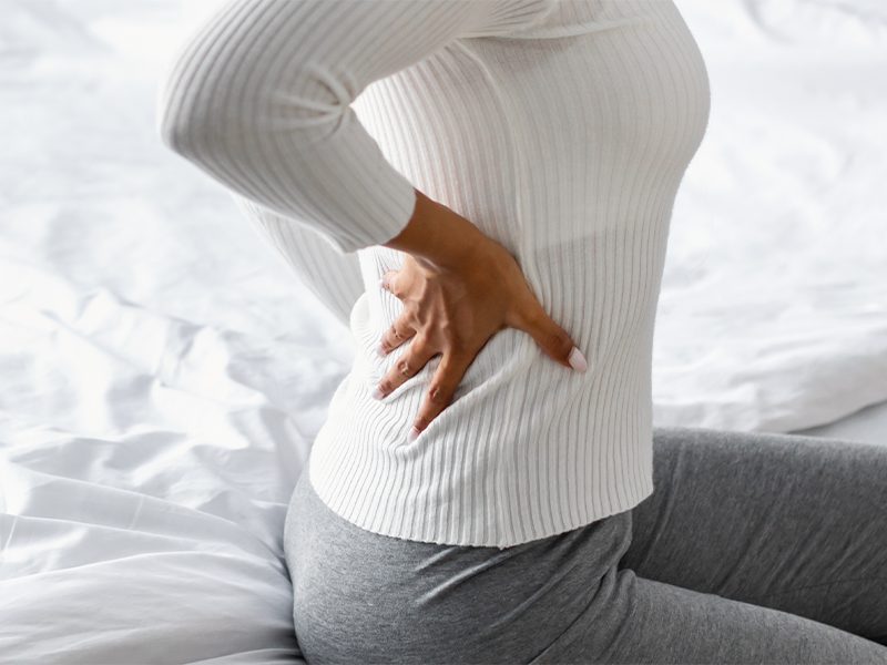 woman sitting on bed with lower back pain