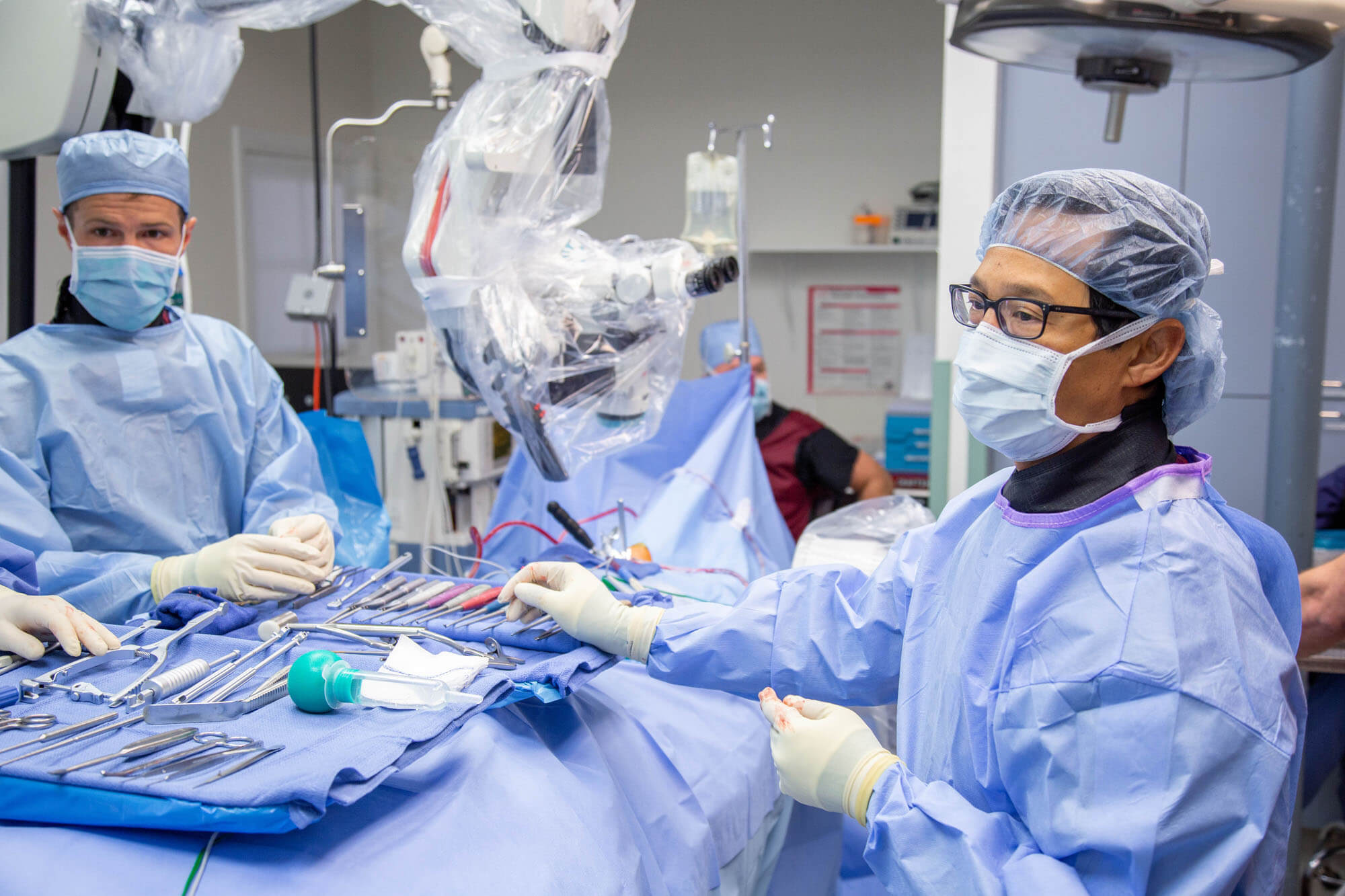 Doctors standing next to table of tools while working in the operating room