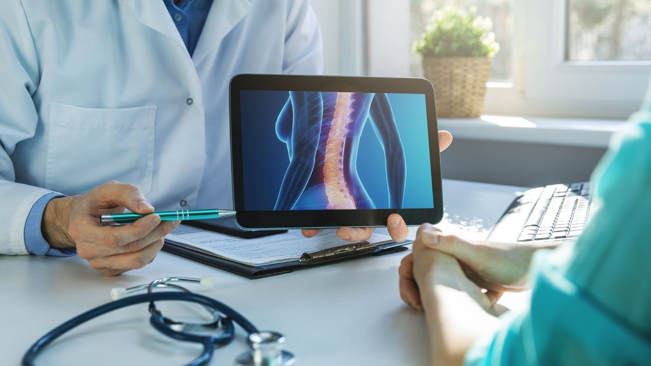 A Doctor Shows A Patient A Picture Of Their Spine On A Tablet